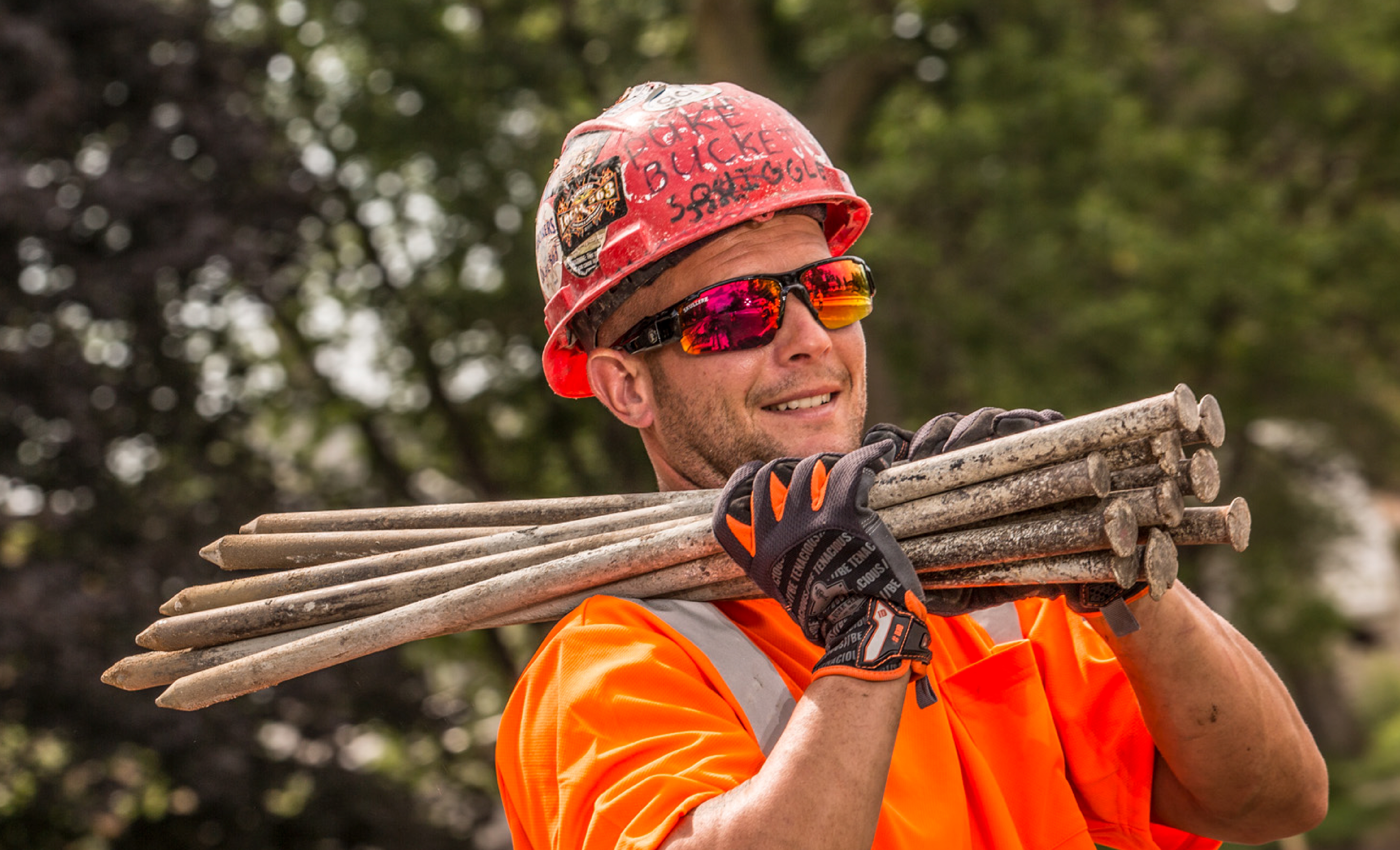 Worker wearing a hard hat and safety gloves while carrying construction stakes over the shoulder