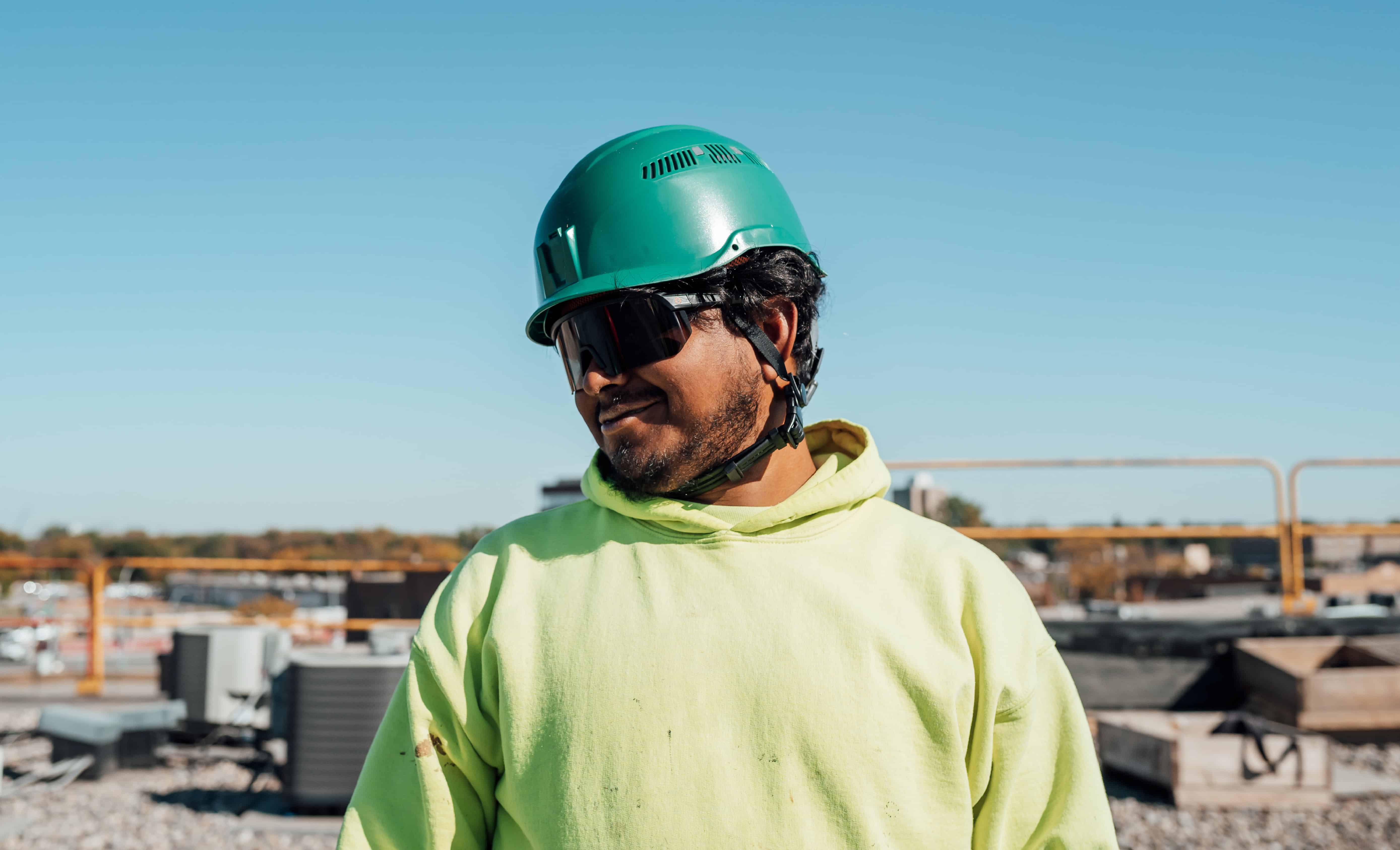Roofing worker wearing AEGIR safety glasses and a green vented safety helmet