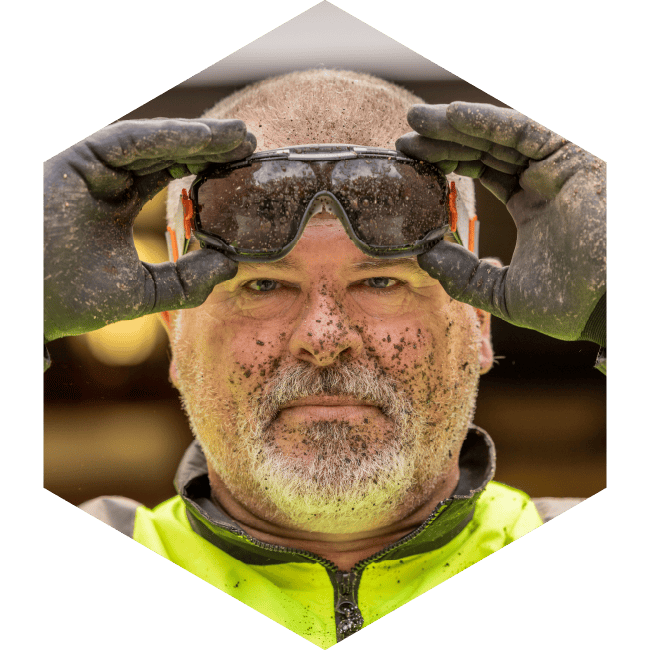 Person removing safety goggles from their face which is covered in dirty except for the part that was protected by goggles