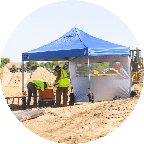 Workers underneath the shade of a Shax Pop-Up Tent, and grabbing cold water bottles from a Chill-Its 5171 cooler