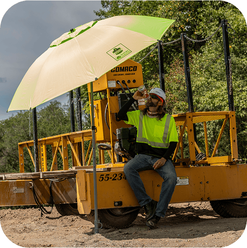 Construction worker resting in the shade and having a drink of water, under a SHAX 6199 Umbrella