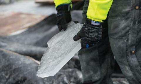 Worker in frigid conditions handling ice with winter work gloves.