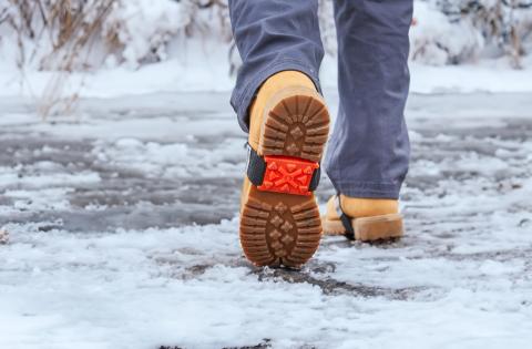 someone wearing a mid-foot ice cleat while walking in the snow