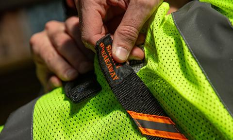 Worker holding breakaway safety straps across shoulders