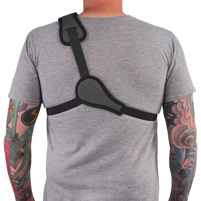 Back view of person in gray t-shirt wearing a black diagonal shoulder strap and chest harness, with tattooed forearms visible.