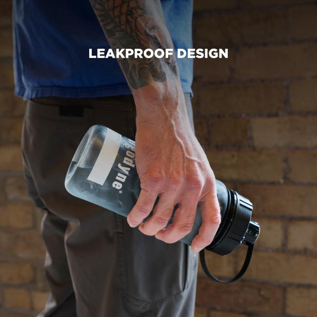 Close-up of tattooed forearm and hand holding a clear water bottle with a black cap and strap against a brick wall; "LEAKPROOF DESIGN" text overlay