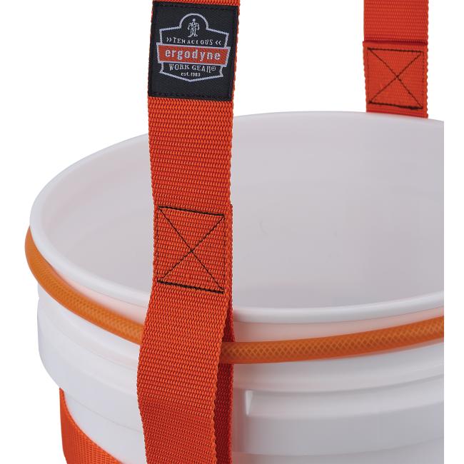 Close-up of white plastic bucket rim with orange woven strap and orange textured handle; strap has black fabric label and reinforced X stitching.