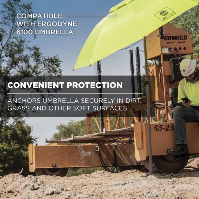 Lime safety umbrella mounted on orange construction lift beside seated worker in hard hat, stake anchored in dirt