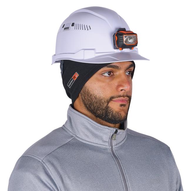 White safety hard hat with orange-and-black mounted headlamp worn by a man wearing a black head liner and gray zippered jacket.