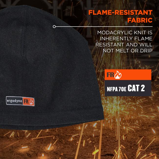 Close-up of black knit beanie with vertical seam and small orange/white fire label, set against sparks and visible "flame-resistant fabric" signage.