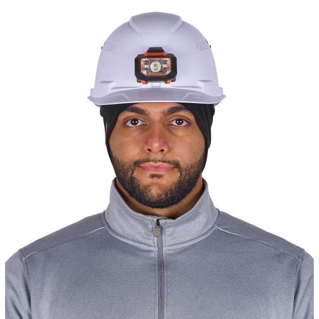Close-up of person's face wearing a white hard hat with an orange-black headlamp, black head covering and gray zip-up jacket.