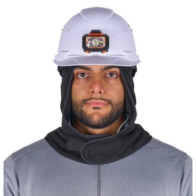 Close-up of person wearing white hard hat with black-and-orange front headlamp, black hood and gray zip jacket, showing eyes and lower face.