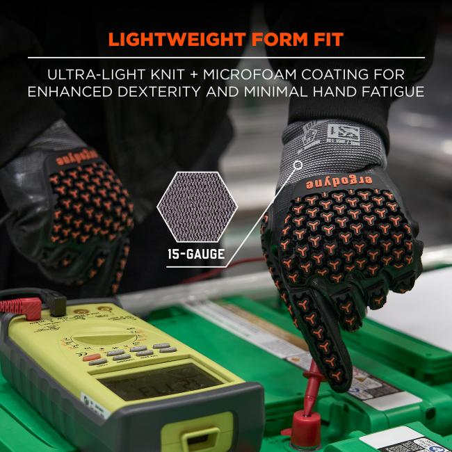 Close-up of a gray and black glove with orange textured grip, red probe attached to a yellow multimeter resting on a green case