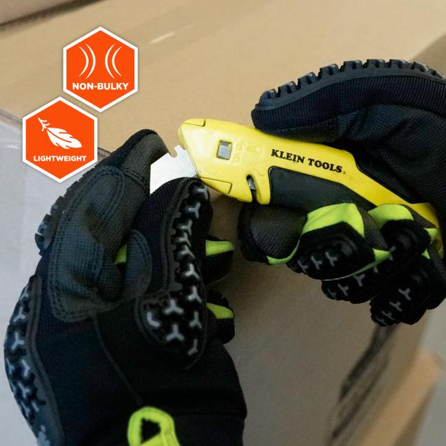 Black and neon-green work gloves holding a yellow utility knife with exposed blade; orange hexagon icons reading "NON-BULKY" and "LIGHTWEIGHT" on cardboard background.
