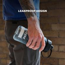 Close-up of tattooed forearm and hand holding a clear water bottle with a black cap and strap against a brick wall; "LEAKPROOF DESIGN" text overlay