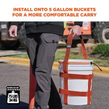 Person's lower torso and hand holding orange webbing harness attached to a white plastic bucket