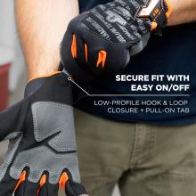 Close-up of black and gray work gloves with orange accents being pulled onto a person's hand, showing hook-and-loop closure and printed text