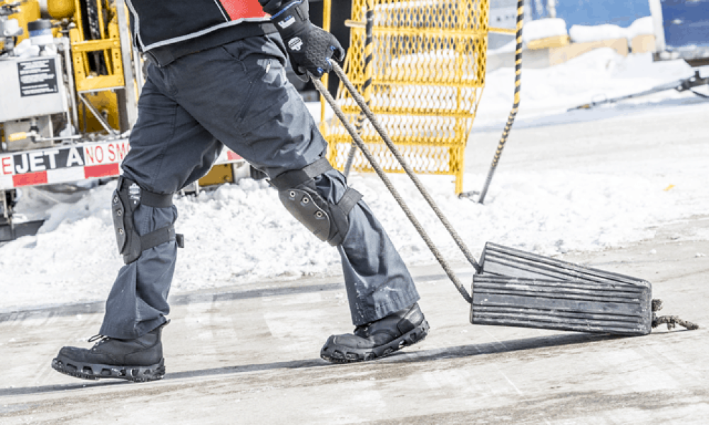 Worker dragging gear on tarmac with kneepads on