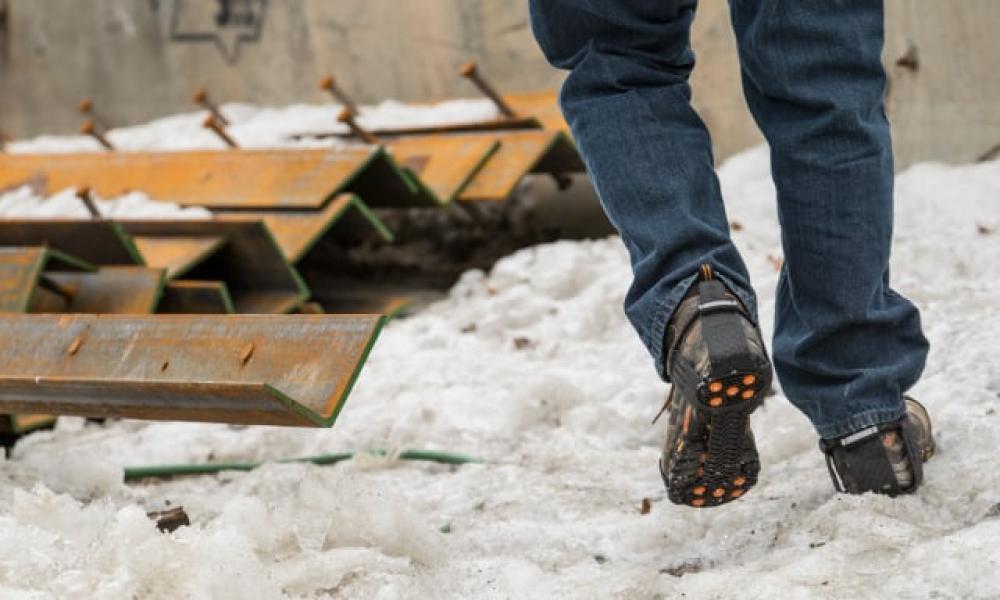 On jobsite, worker with ice traction walks new plows