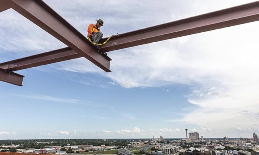 Worker relaxing at height on I Beams, with supporting tethers.