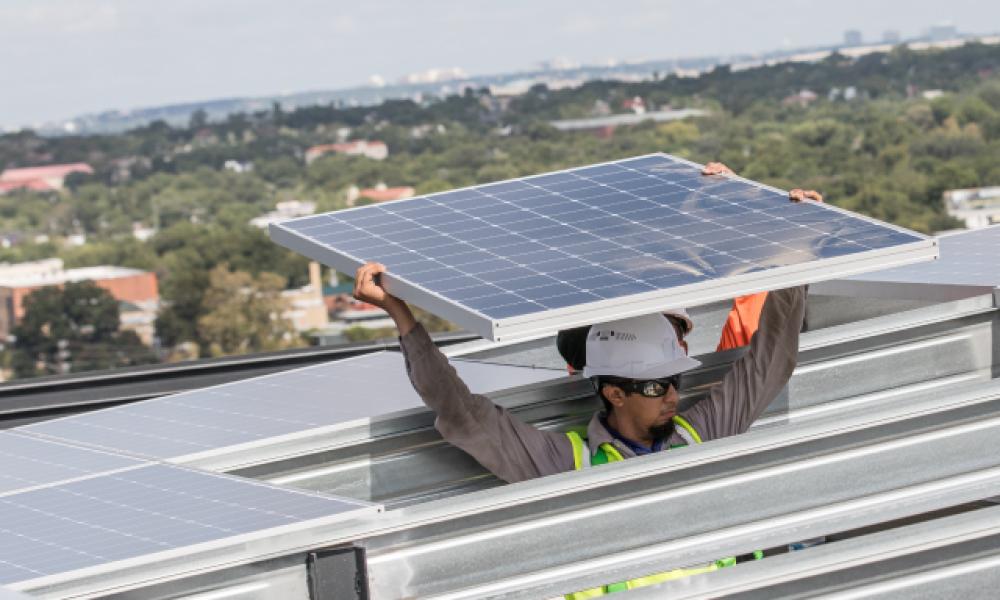 Worker with protective hard hat carrying solar panels overhead