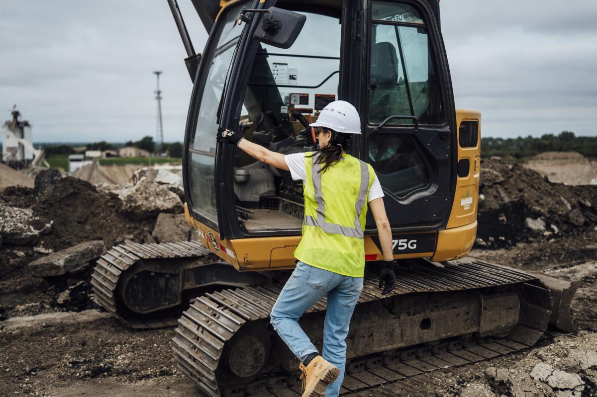 Worker wearing hi-vis vest, climbing into excavator on a job site