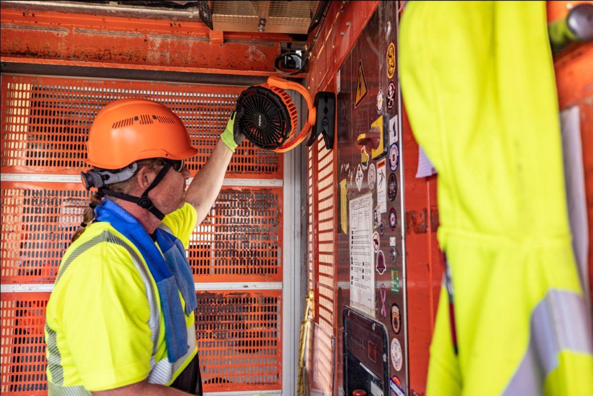 Construction worker adjusting portable fan on worksite