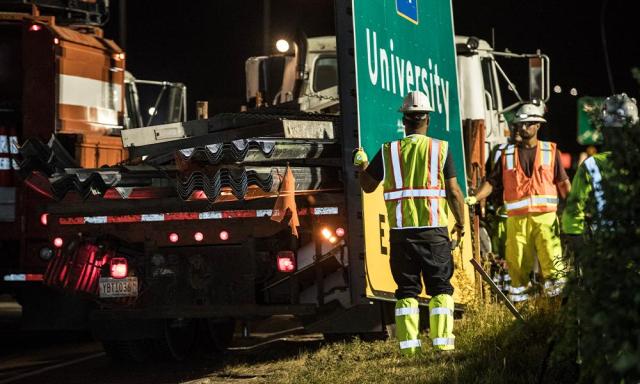 Two workers setting up a highway sign in hi-vis gear at night